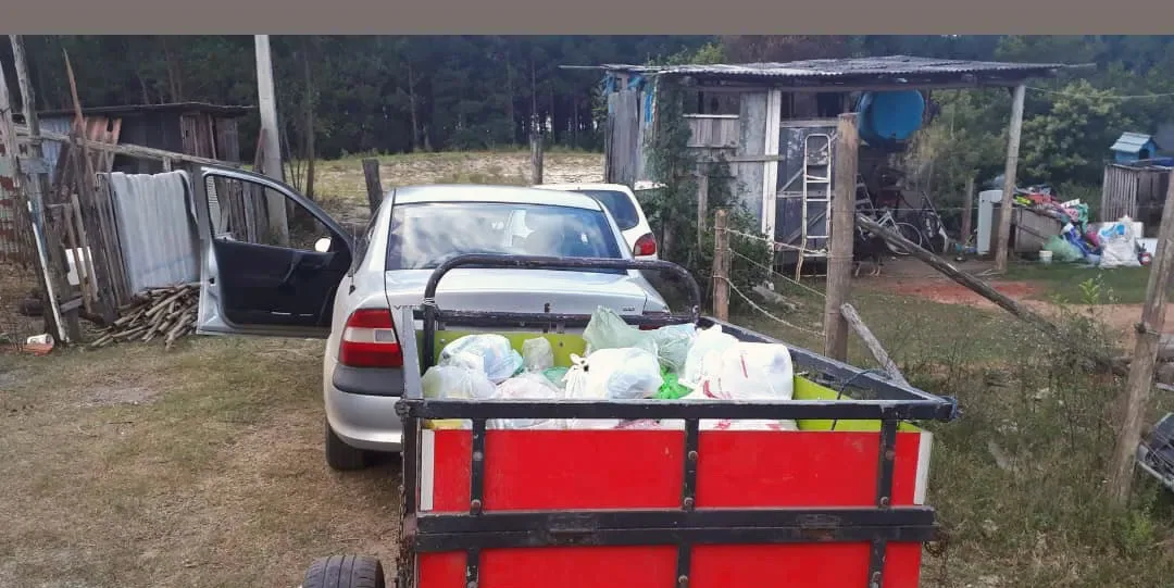 Carro com carretinha carregada de sacolas de alimentos em um terreno no bairro