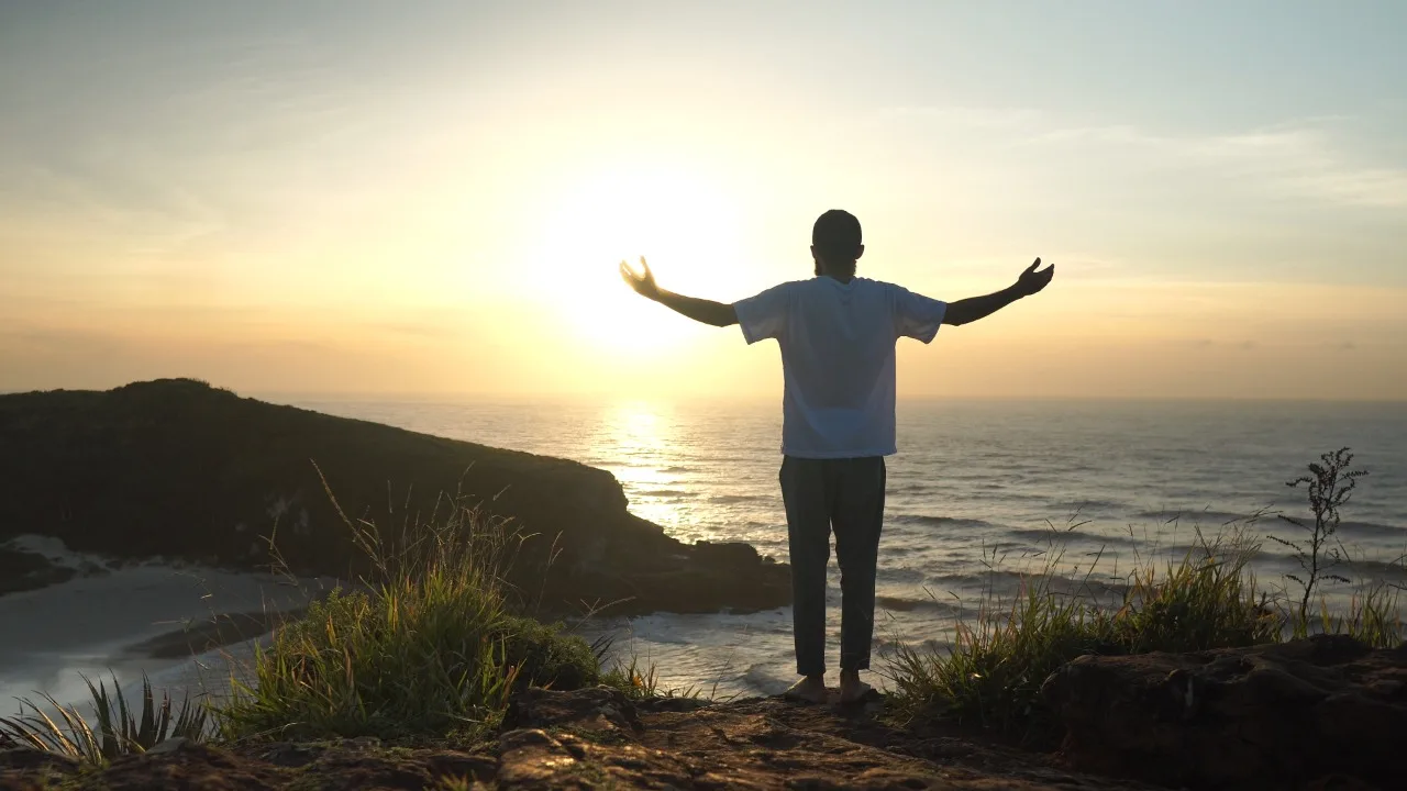 Eduardo de braços abertos para o nascer do sol nas falésias de Torres